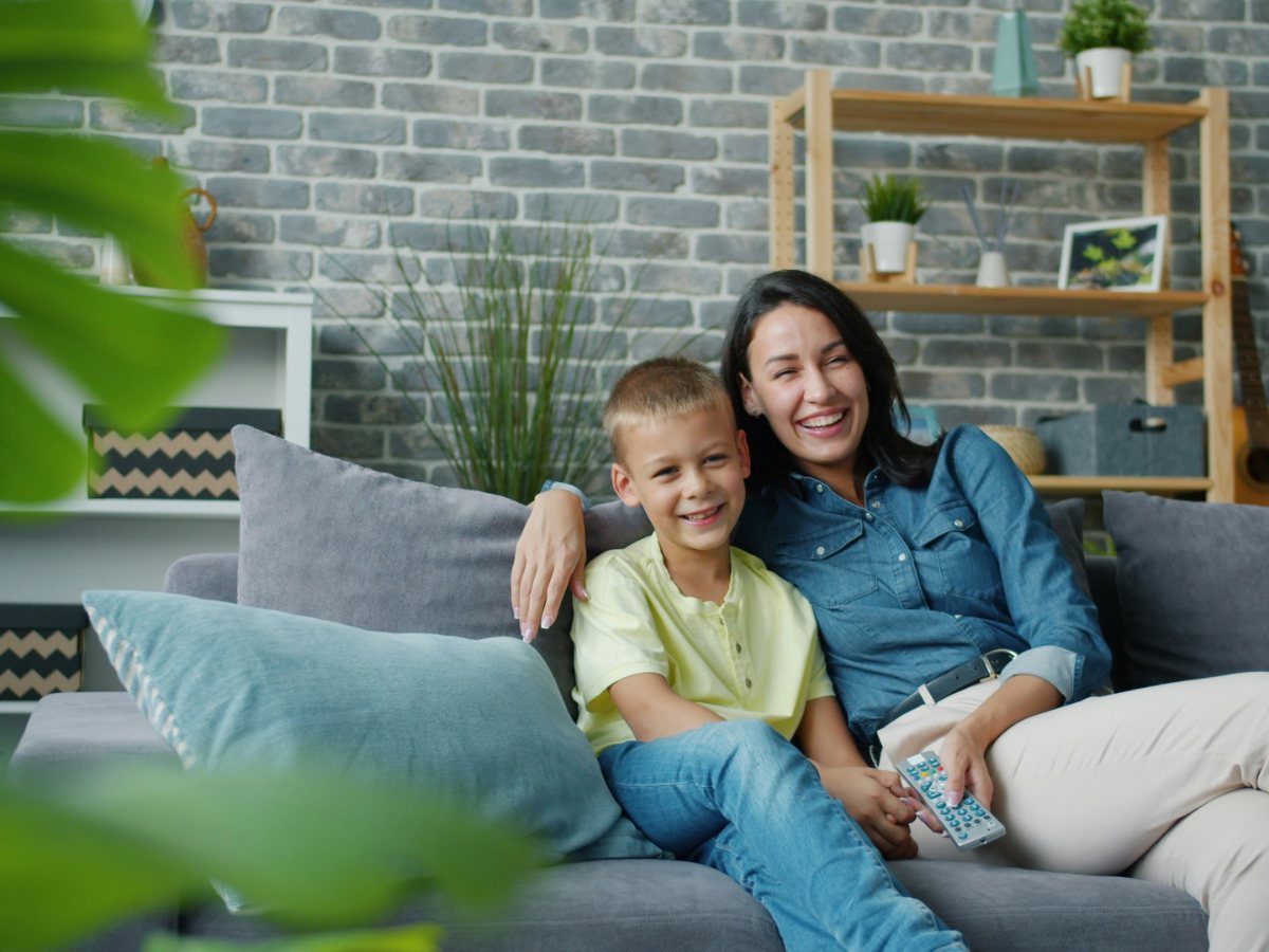 A parent and child watching television together on the sofa